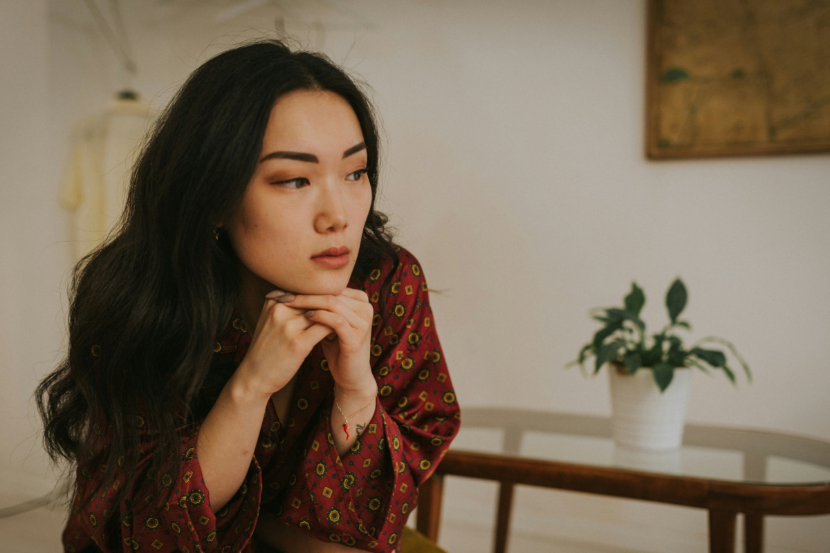 Woman sitting indoors, looking to the side in quiet reflection, natural light