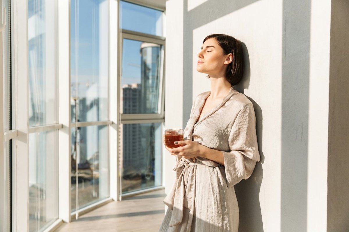 Woman standing in bright natural light with eyes closed, holding a warm drink, expressing quiet relief and emotional regulation — EMDR intensive therapy Singapore